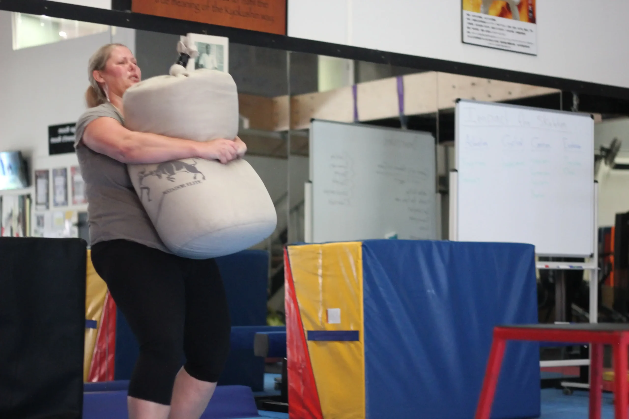 Woman carrying a heavy sandbag during a women-only fitness class at Functional Fitness Eltham, Australia, focusing on strength and endurance Woman carrying a heavy sandbag during a women-only fitness class at Functional Fitness Eltham, Australia, focusing on strength and endurance