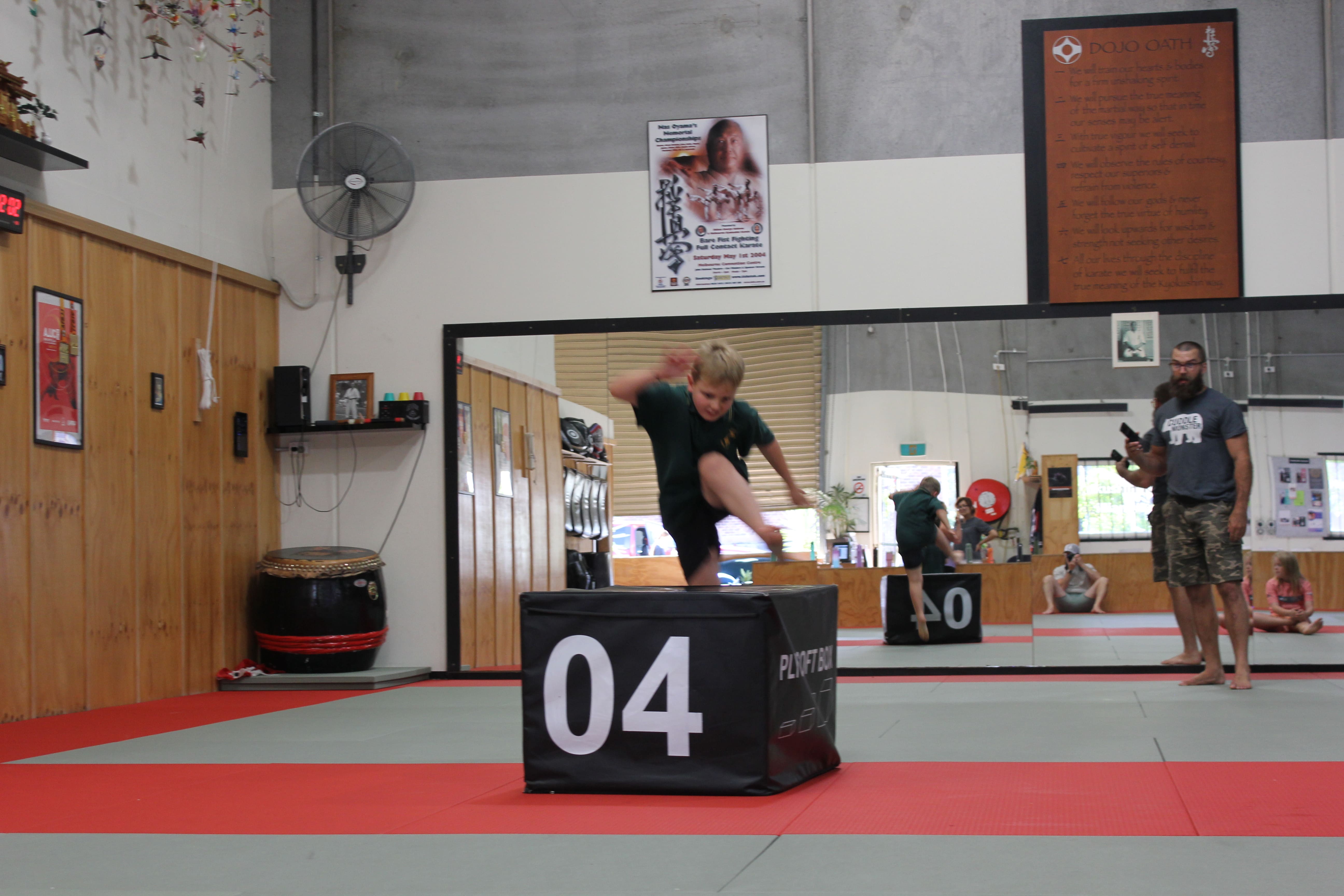 A neurodivergent child jumping onto a soft plyo box during a structured kids fitness session at Functional Fitness Eltham, supervised by an experienced coach.