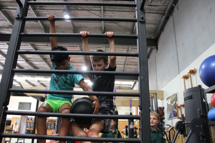 Two neurodivergent kids with ADHD or autism working together to climb and lift a medicine ball during a functional fitness class at Functional Fitness Eltham.